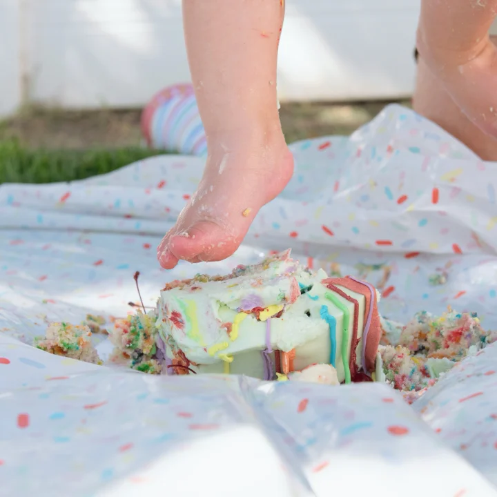 A baby stepping into their cake during their first birthday party
