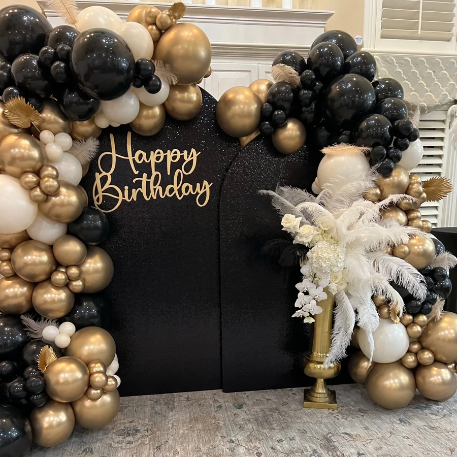 Black and gold balloon garland surrounding a Happy Birthday backdrop with feather accents