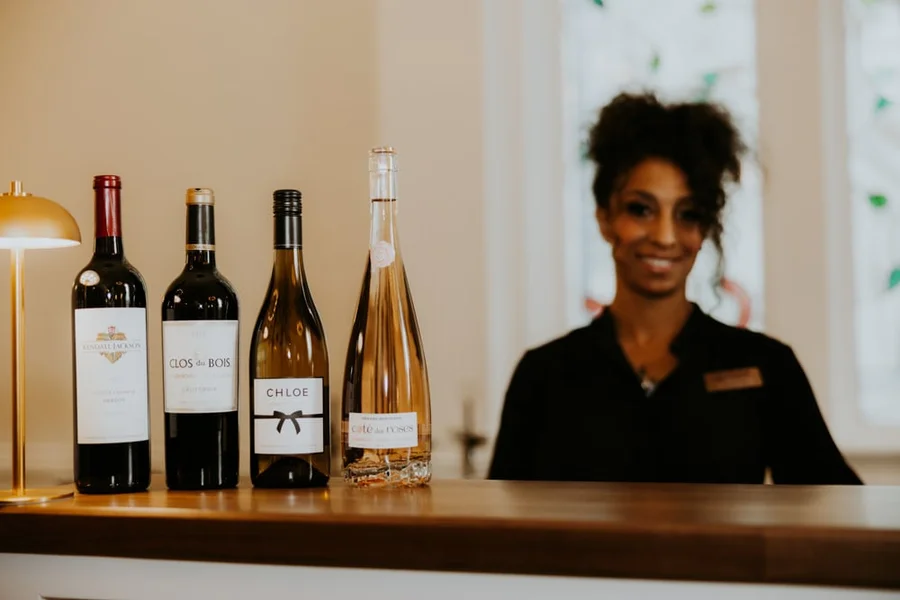 Smiling bartender behind a counter with wine bottles lined up in front