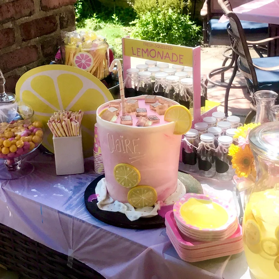 Lemonade-themed party table with a pink cake, lemon decor and drink jars