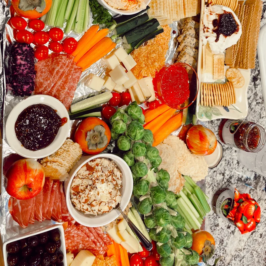 Grazing board with fresh vegetables, fruit, dips and crackers on a marble counter