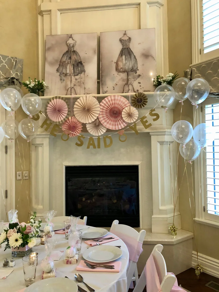 Bridal shower room with pink paper fans, balloons and white tables below a fireplace