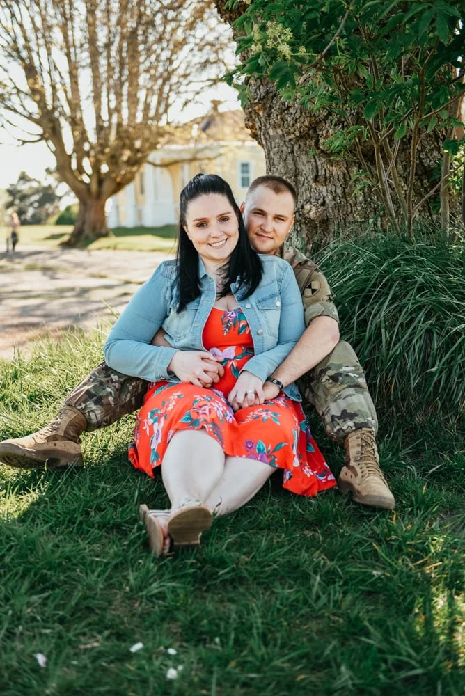 Couple seated on grass, the woman in a red floral dress and the man in fatigues