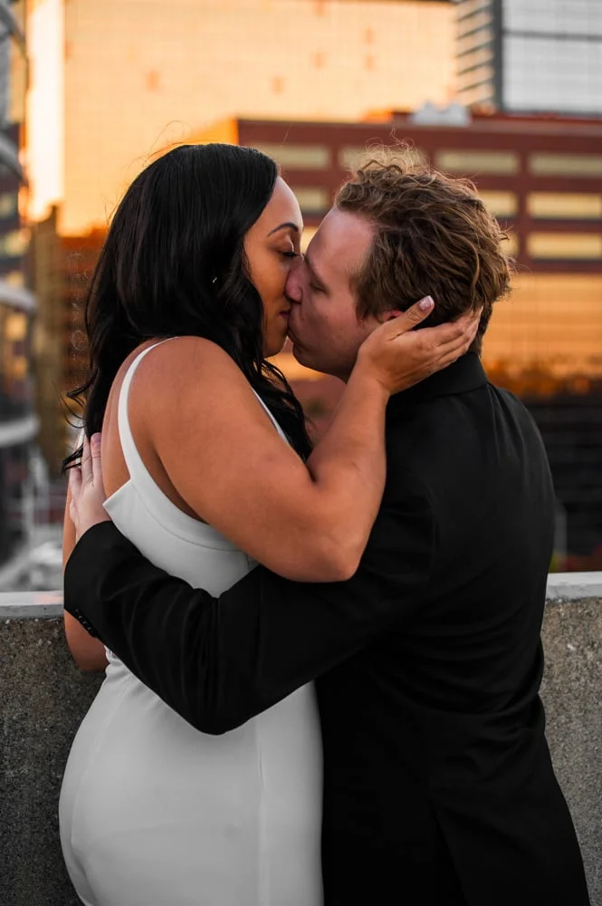 Couple sharing a kiss on a city rooftop at sunset for their engagement session