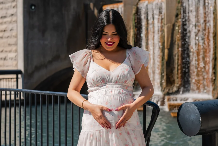 Maternity portrait of a woman in a white tulle gown by a waterfall wall