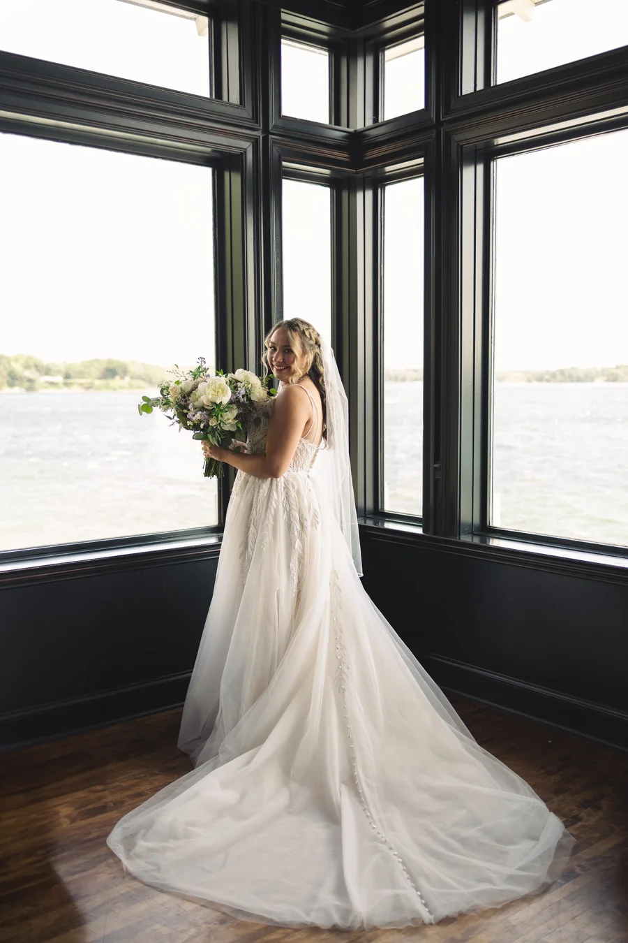 Bride holding a bouquet in a corner window, her gown train spread on the floor