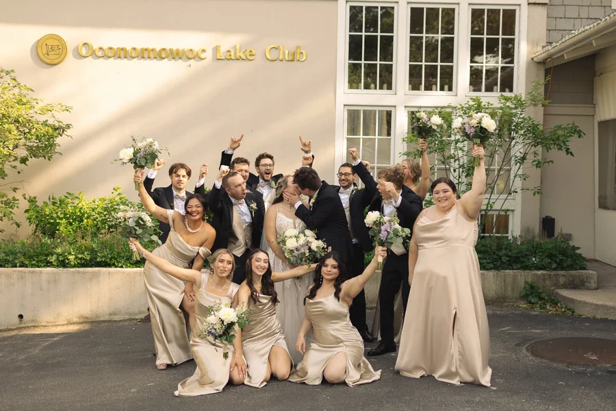 Wedding party in champagne dresses and black suits cheering with bouquets outside a club