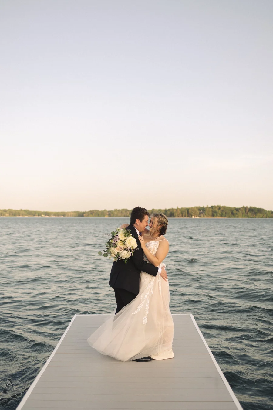 Couple kissing on a wooden dock surrounded by calm lake water