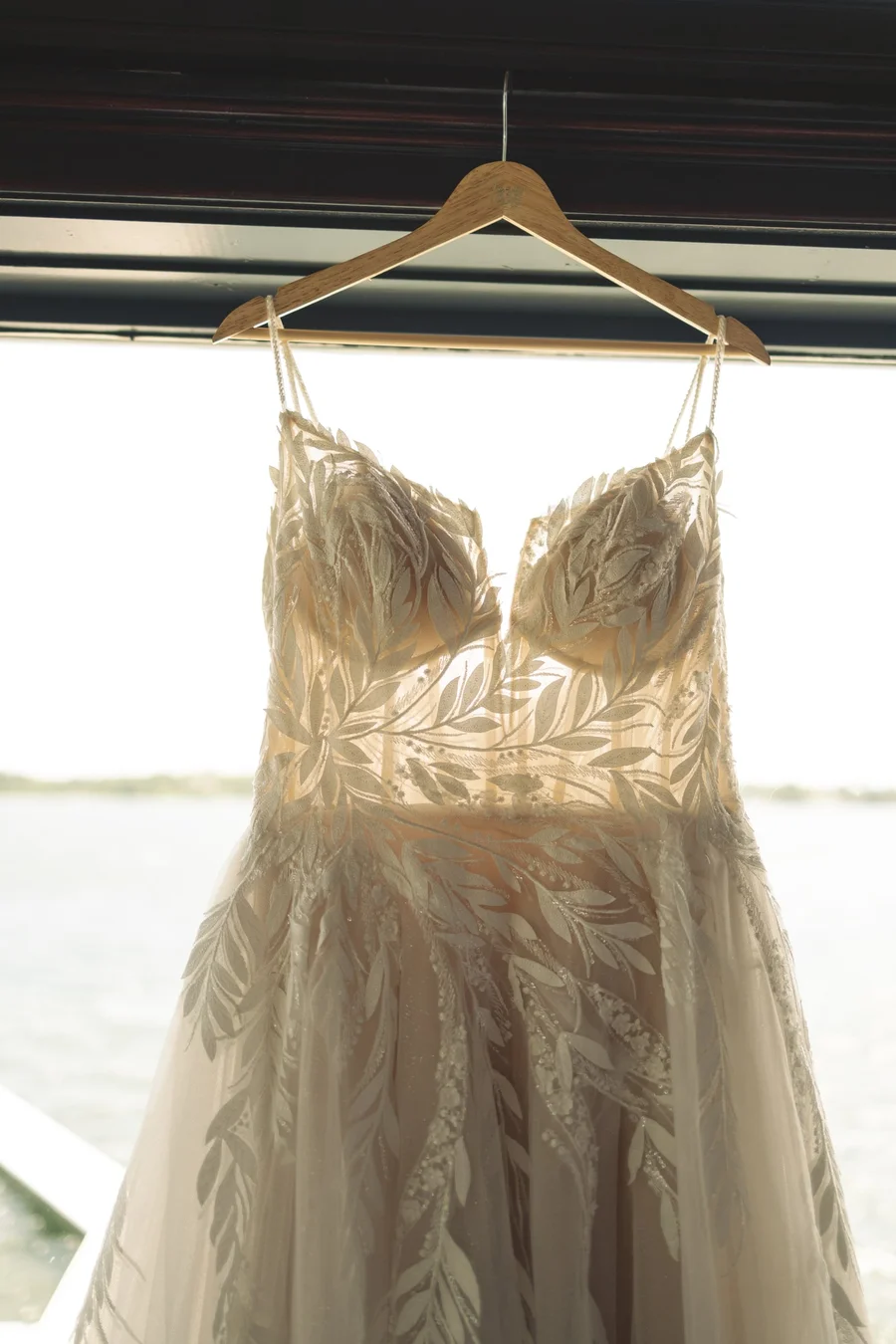 Lace wedding gown hanging on a hanger in front of a lake window