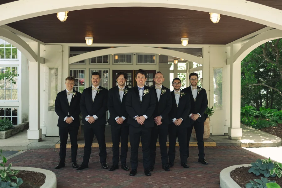 Groomsmen in black suits lined up under a covered entrance
