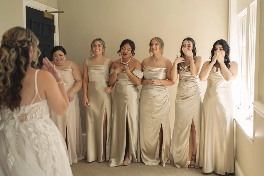 Bridesmaids in champagne dresses reacting emotionally as they see the bride